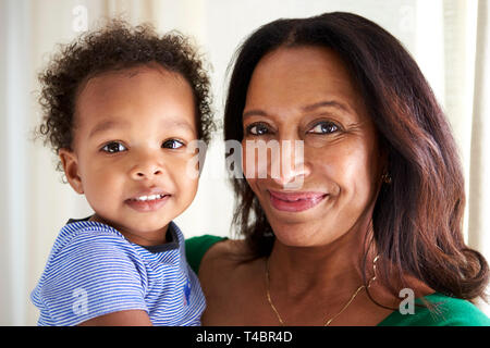 Happy mixed race middle aged grandmother holding her two year old grandson, both looking to camera smiling, close up, head and shoulders Stock Photo