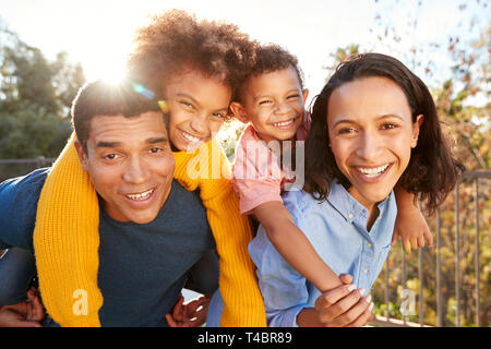 Young mixed race parents parents having fun piggybacking their children in the garden and looking to camera, close up Stock Photo
