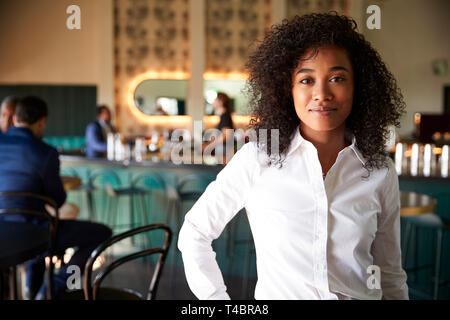 Female Manager Of Busy Cocktail Bar In Restaurant With Customers At Camera Stock Photo