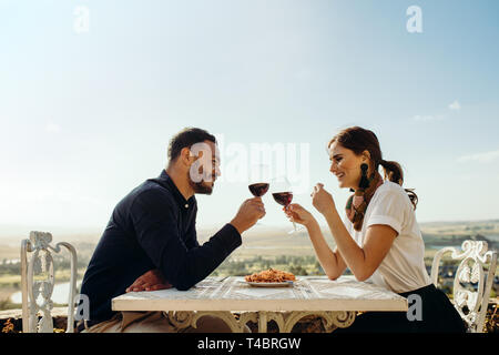 Smiling couple sitting at a restaurant toasting glass of red wine. Happy couple on a date talking to each other holding glass of wine. Stock Photo