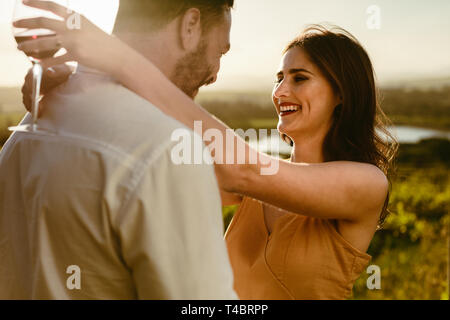 Couple in love standing together holding each other. Side view of a smiling woman standing with her boyfriend holding a wine glass with her arms aroun Stock Photo