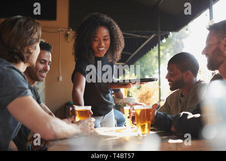 Waitress Serving Drinks To Group Of Male Friends Meeting In Sports Bar Stock Photo
