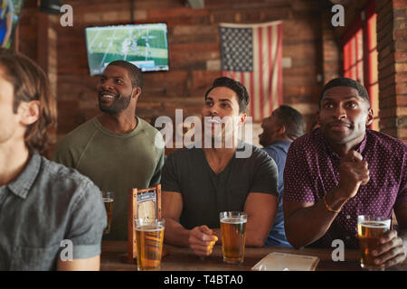 Male Friends Drinking Beer And Watching Game On Screen In Sports Bar Stock Photo