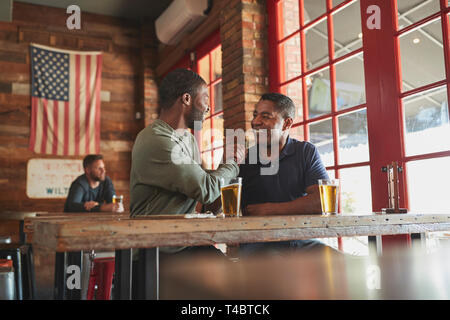 Two Male Friends Greeting One Another In Sports Bar Enjoying Drink Together Stock Photo