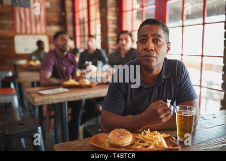 Man Watching Game On Screen In Sports Bar Eating Burger And Fries Stock Photo