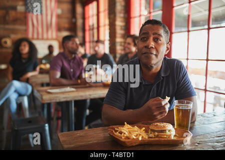 Man Watching Game On Screen In Sports Bar Eating Burger And Fries Stock Photo