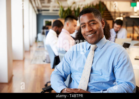 Portrait Of Mature Businessman In Modern Office With Colleagues Meeting Around Table In Background Stock Photo