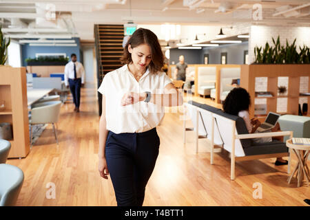 Businesswoman Walking Through Modern Office Checking Health Data On Smart Watch Stock Photo