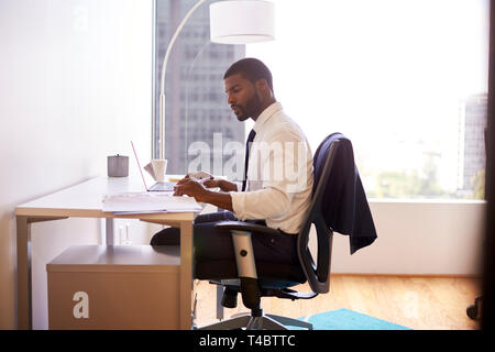 Businessman Sitting At Desk Working On Laptop In Modern Office Stock Photo