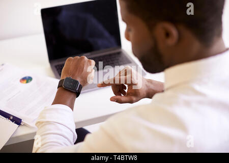 Businessman Working On Laptop At Desk In Modern Office Checking Data On Smart Watch Stock Photo