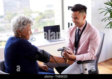 Male Doctor In Office Checking Senior Female Patients Blood Pressure Stock Photo
