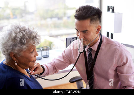 Male Doctor In Office Listening To Senior Female Patients Chest Using Stethoscope Stock Photo