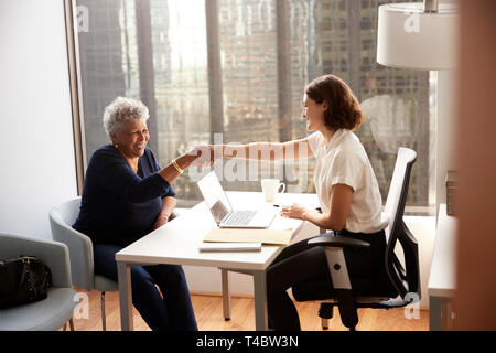 Senior Woman Shaking Hands With Female Doctor In Hospital Office Stock Photo