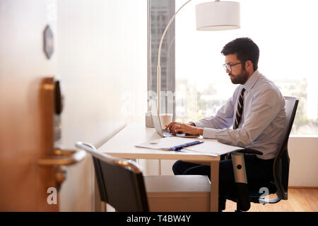 Businessman Sitting At Desk Working On Laptop In Modern Office Stock Photo