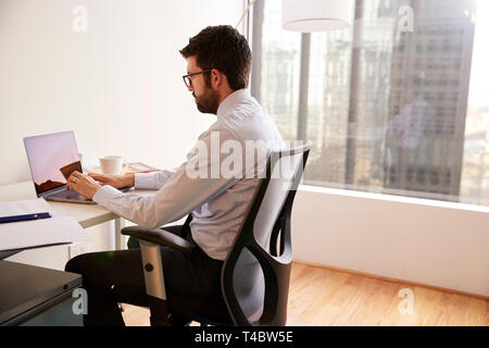 Businessman Sitting At Desk Working On Laptop In Modern Office Stock Photo