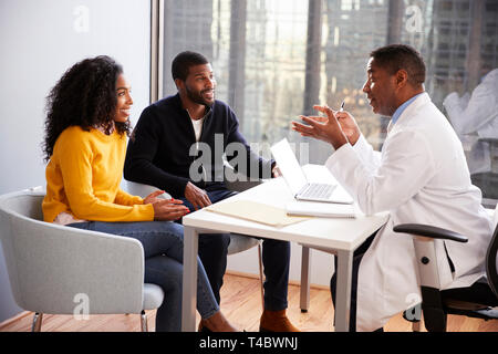 Smiling Couple Having Consultation With Male Doctor In Hospital Office Stock Photo