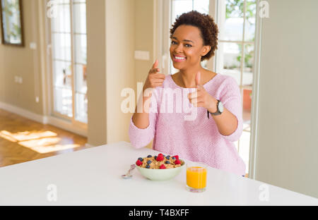 Young african american woman having healthy breakfast in the morning at home pointing fingers to camera with happy and funny face. Good energy and vib Stock Photo