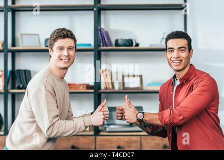 Two smiling multiethnic  friends showing thumbs up and looking at camera Stock Photo