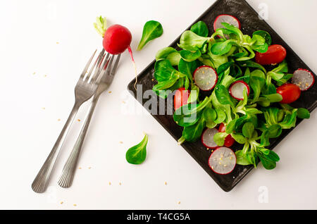 Healthy breakfast or lunch. Fresh vegetable salad of radish, tomatoes and corn salad or Valerianella locusta on black plate. Diet and vegetarian eatin Stock Photo