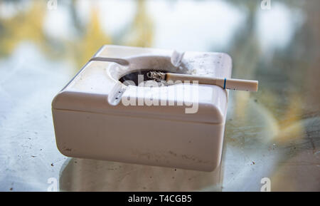 Cigarette burning in white ashtray Stock Photo