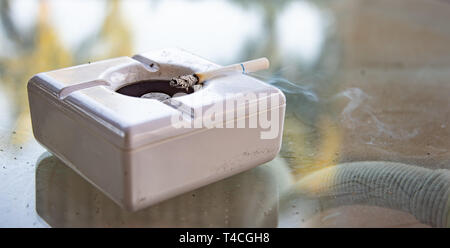 Cigarette burning in white ashtray Stock Photo