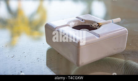 Cigarette burning in white ashtray Stock Photo