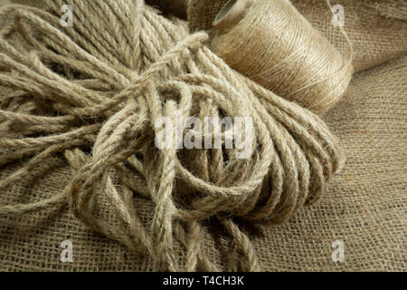 Two spools of burlap threads or jute twine and coil of linen rope on sackcloth fabric in close-up on grey background Stock Photo