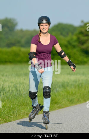 Young woman wearing a helmt and protectors rollerblading on a small road. Stock Photo