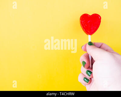 A woman with green painted nails with a red lollipop in her hand and yellow background Stock Photo