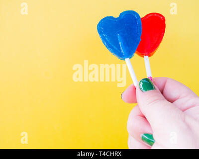 A woman with green painted nails with two different lollipop in her hand and yellow background Stock Photo