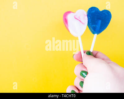 A woman with green painted nails with two different lollipop in her hand and yellow background Stock Photo