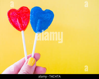 A woman with green painted nails with two different lollipop in her hand and yellow background Stock Photo