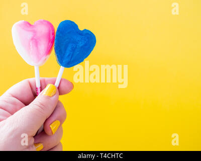 A woman with green painted nails with two different lollipop in her hand and yellow background Stock Photo