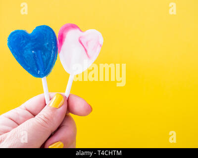 A woman with green painted nails with two different lollipop in her hand and yellow background Stock Photo