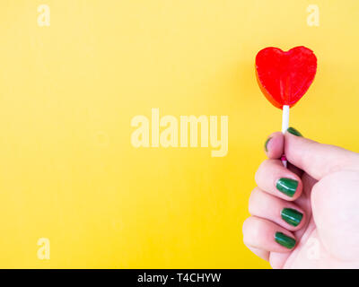 A woman with green painted nails with a red lollipop in her hand and yellow background Stock Photo