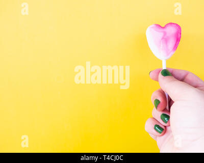 A woman with green painted nails with a lollipop in her hand and yellow background Stock Photo