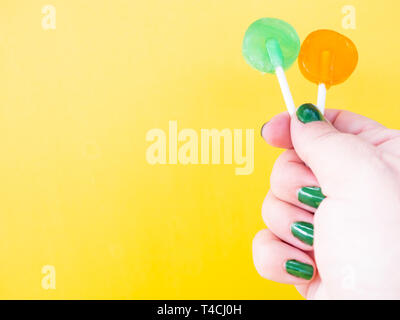 A woman with green painted nails with two different lollipop in her hand and yellow background Stock Photo