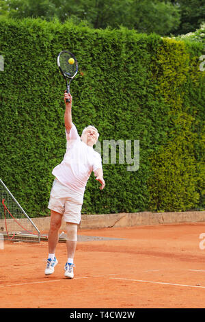 Old active man serving ball on tennis match Stock Photo