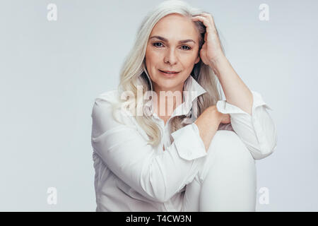 Attractive senior woman sitting over white background. Mature caucasian woman sitting relaxed in studio. Stock Photo
