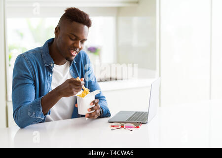 Handsome young african business man eating delivery asian food and working using computer concentrated Stock Photo