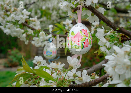 Decorative Easter egg hanging on flowering cherry tree with white flowers. Easter banner background Stock Photo