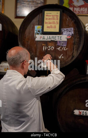 Malaga,Spain 04.04.2019: Bar tender pour the famous pajarete spanish wine from Sherry Barrels in the famous authentic Bodega Antigua Casa de Guardia Stock Photo