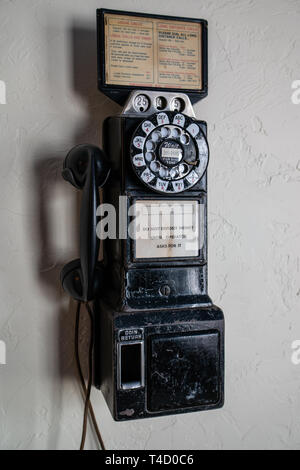 April 15, 2019 Cottage Grove Oregon USA -  A black used vintage pay phone with rotary dial and coin slots hangs on a wall ready to be used. Stock Photo