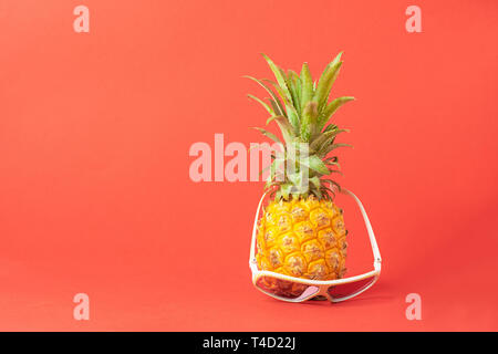 Ripe pineapple in sunglasses on a trendy coral background. Summer holiday concept. Minimalism. Horizontal frame. Stock Photo