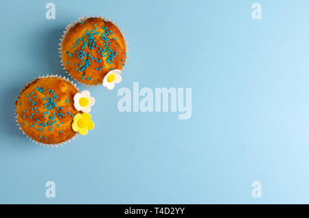 Muffins decorated with flowers of mastic on pastel blue background. Top view. Copy space. Easter Holidays and greeting card concept. Stock Photo