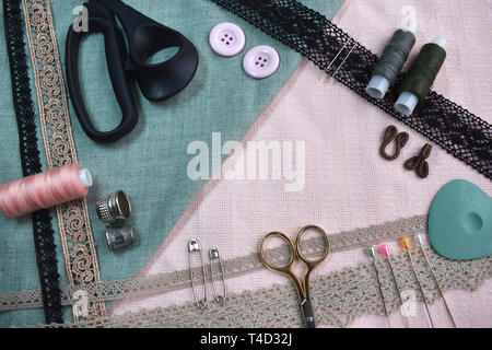 Sewing scene table flat lay composition. Threads, lace, pins, scissors, tape, reel, cloth. Pastel colors rose pink light blue material linen fabric Stock Photo