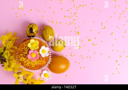 Muffins decorated with sprinkles, flowers of mastic and yellow easter quail eggs on pastel pink background. Top view. Copy space. Easter Holidays and  Stock Photo