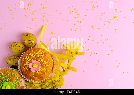 Muffins decorated with sprinkles, flowers of mastic and yellow easter quail eggs on pastel pink background. Top view. Copy space. Easter Holidays and  Stock Photo