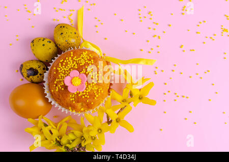 Muffins decorated with sprinkles, flowers of mastic and yellow easter quail eggs on pastel pink background. Top view. Copy space. Easter Holidays and  Stock Photo