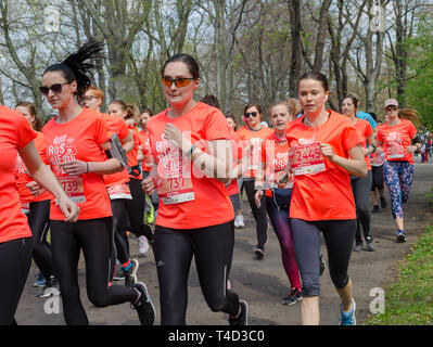 Huge group of women in orange t-shirts with numbers run marathon in the park in spring. Wroclaw, Poland - April 7, 2019. Stock Photo